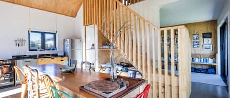 A modern kitchen with a wooden island, a dining area with mismatched chairs, and a staircase with a wooden railing.