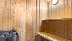 Una sauna con paredes de madera, un banco y un recipiente metálico con piedras.
