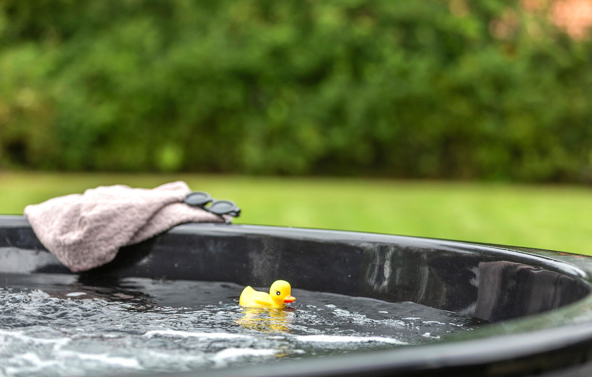 A hot tub with a rubber duck floating in the water, a pair of sunglasses, and a towel on the edge.