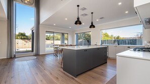 Une cuisine moderne dotée d’un grand îlot central, bénéficiant d’un éclairage naturel abondant et offrant une vue sur le jardin arrière.