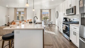 A modern kitchen with white cabinetry, a central island, stainless steel appliances, and pendant lighting. - Skyline 1649, Hot Tub, Nintendo Switch, Community Amenities! (Washington)