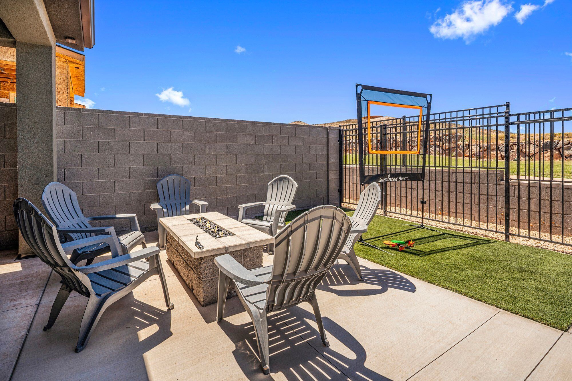 An outdoor patio with a table and chairs, a basketball hoop, and a fenced area with artificial turf.