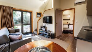 Een moderne woonkamer met een bank, een salontafel en een televisie. Een trap leidt naar een keuken en een badkamer.