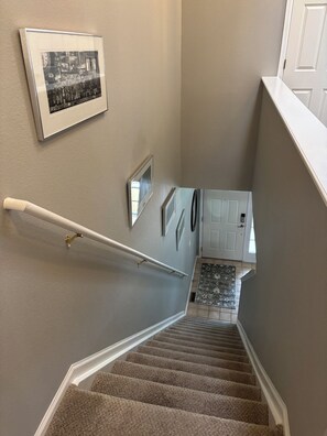 Een betegelde trap met een leuning, een lijst met een afbeelding aan de muur, en een deur bovenop.
