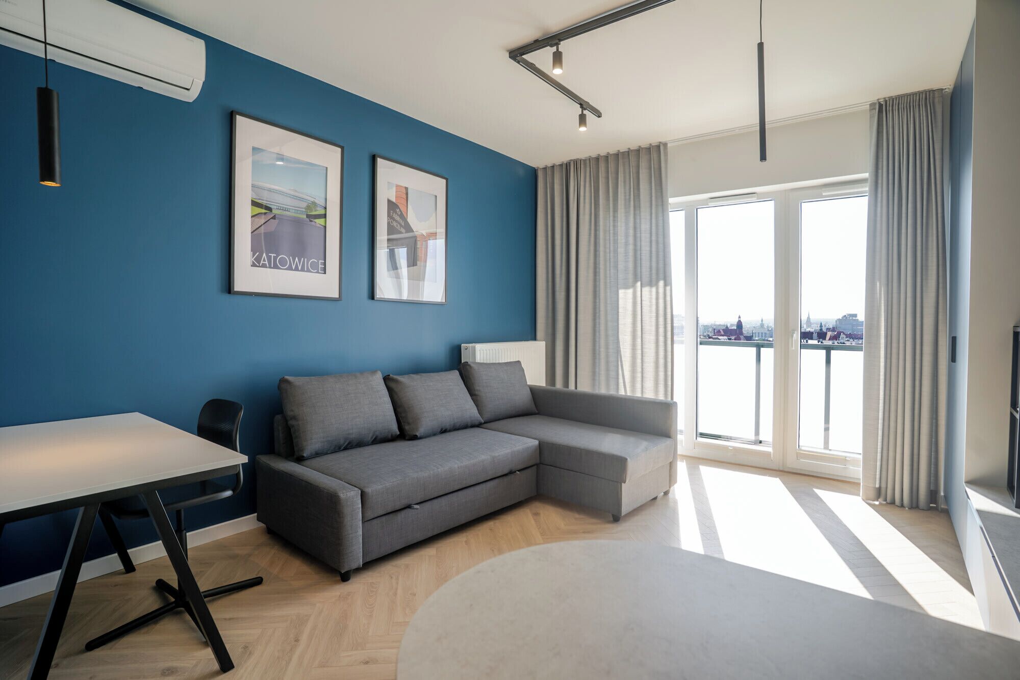 Una sala de estar moderna con un sofá seccional gris, una mesa blanca y un ventanal con vista a la ciudad.