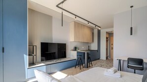 A modern hotel room with a large bed, a small kitchenette, a dining area, and a bathroom.