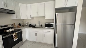 Una cocina moderna con armarios blancos, un refrigerador de acero inoxidable, un microondas, una estufa y una cafetera.