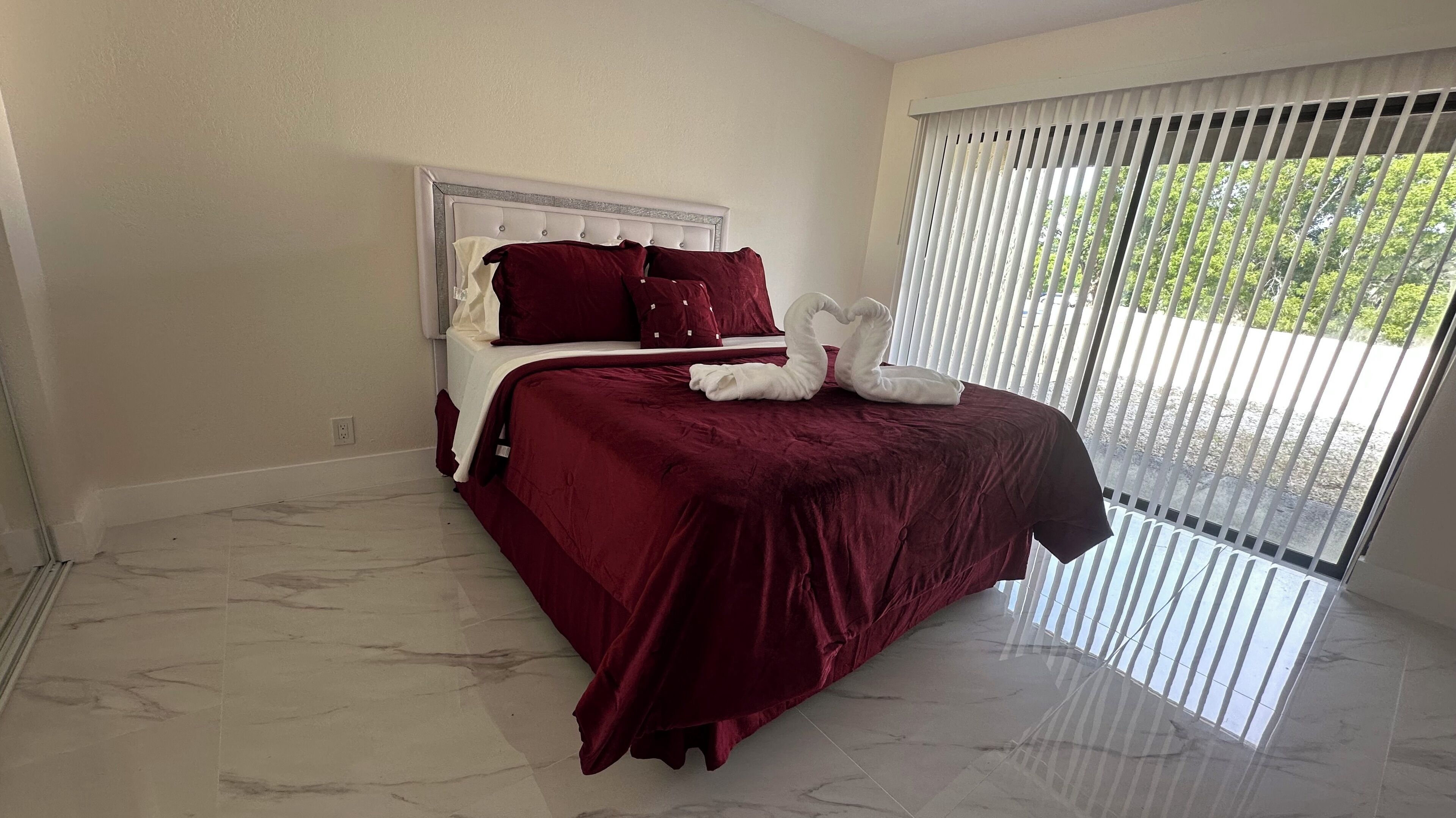 A bedroom with a bed, white headboard, red bedding, and a swan decoration.