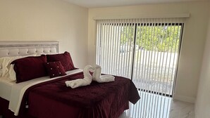 Un dormitorio con cama, cabecera, ventana con persianas y vistas al exterior.