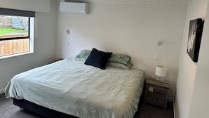 Une chambre à coucher comprenant un lit, une table de chevet, un climatiseur fixé au mur et une fenêtre donnant sur l’extérieur.