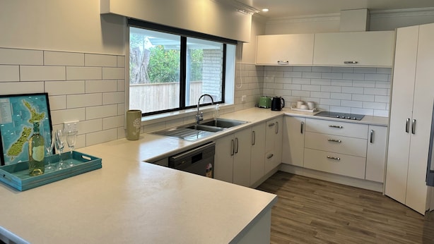 Une cuisine moderne avec des meubles blancs, une grande fenêtre et un plancher en bois.