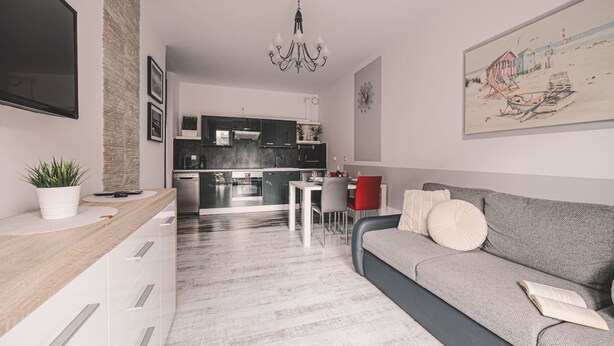 Una sala de estar moderna con un sofá gris, un comedor y una cocina al fondo.