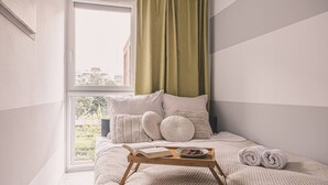 A bedroom with a bed, a window, and a tray with a book and a plate of food.