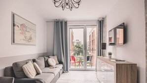 Una sala de estar moderna con un sofá, un televisor de pantalla plana y un balcón con vistas a edificios.