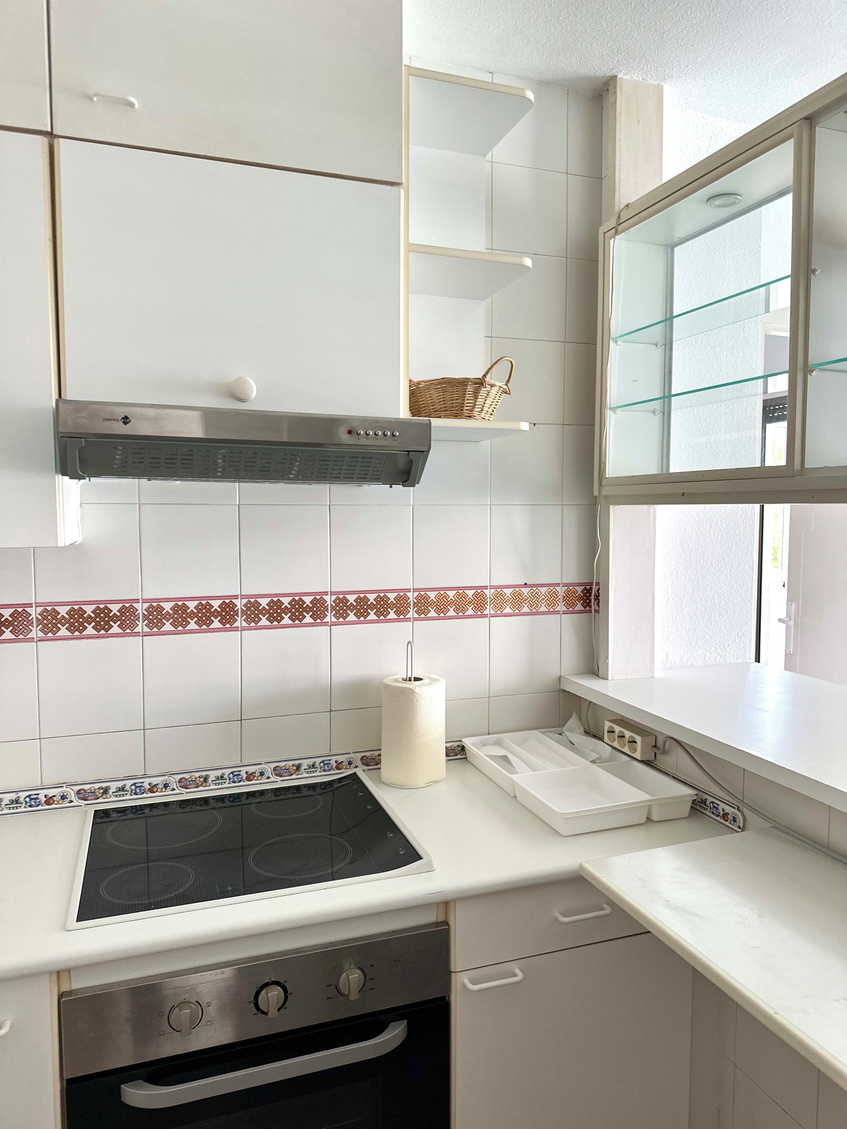 Une cuisine avec des armoires blanches, un four encastré, une plaque de cuisson, une hotte aspirante fixée au mur et une fenêtre donnant sur un beau paysage.