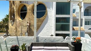 A rooftop terrace with outdoor seating, a heart-shaped window, and a white building with balconies.