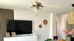 A modern living room with a flat-screen TV, a ceiling fan, and a dining area with a table and chairs.