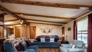 A cozy living room with a wooden ceiling, a large window with curtains, and a view of a body of water. - Charming Canal Waterfront 3/2 in Salt Springs (Salt Springs)