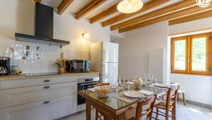 Een moderne keuken met houten balken, een ingebouwde magnetron en een eethoek met een glazen tafel en stoelen.
