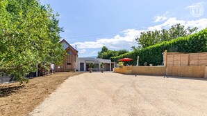 A gravel driveway leading to a modern building with a covered entrance and a red umbrella. - LE REFUGE - DOMESSIN (DOMESSIN)