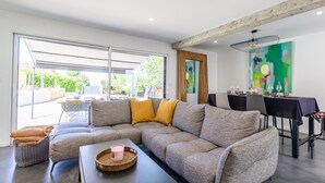 A modern living room with a sectional sofa, a dining table with chairs, and a large window providing a view of the outdoors. - LE REFUGE - DOMESSIN (DOMESSIN)