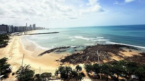 A beach with a city skyline in the background, a rocky area in the foreground, and a clear sky.