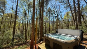 A hot tub in a forested area with trees and a clear sky.