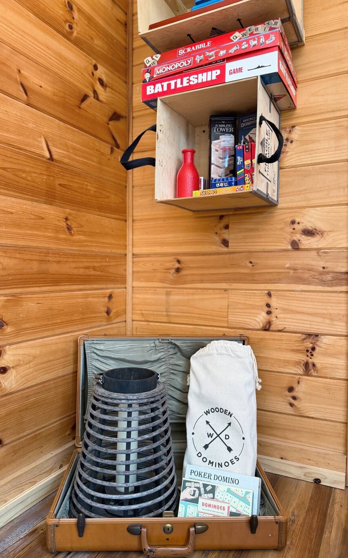 A wooden cabinet with shelves holding board games and a suitcase with poker dominoes.