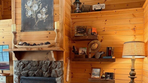 A cozy cabin interior with a stone fireplace, wooden shelves, a leather sofa, and a rustic decor.