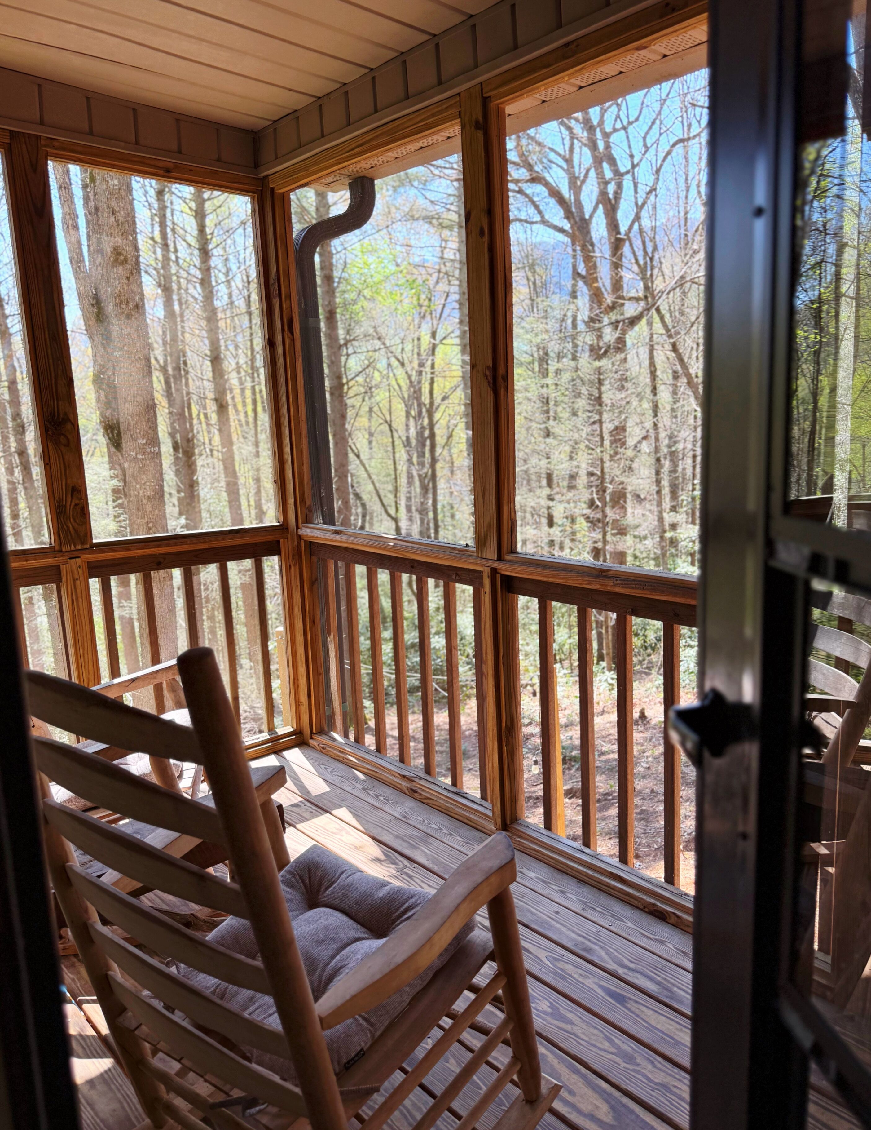 Une terrasse en bois avec un fauteuil à bascule et de grandes fenêtres donnant sur une forêt.