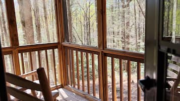 Une terrasse en bois avec un fauteuil à bascule et de grandes fenêtres donnant sur une forêt.