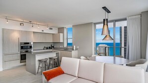 A modern kitchen with a central island, bar stools, and a dining area with a view of the ocean. - Miami Escape, 16th Floor – Near Hollywood Beach (Hollywood)