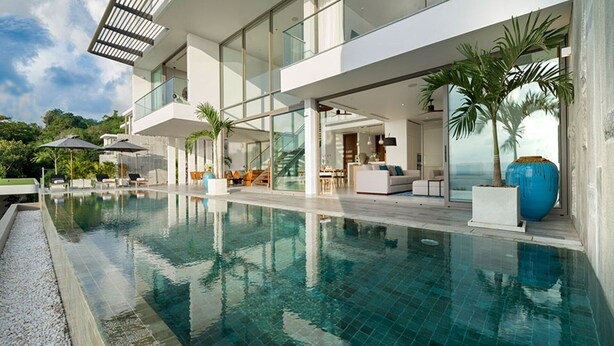 Ett modernt hus med en stor pool, utomhusmöbler och utsikt över havet.