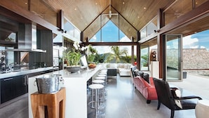Una cocina moderna con barra, una zona de estar con sofá rojo y vistas al cielo y palmeras.