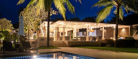 A poolside area with a covered patio, palm trees, and a stone wall.