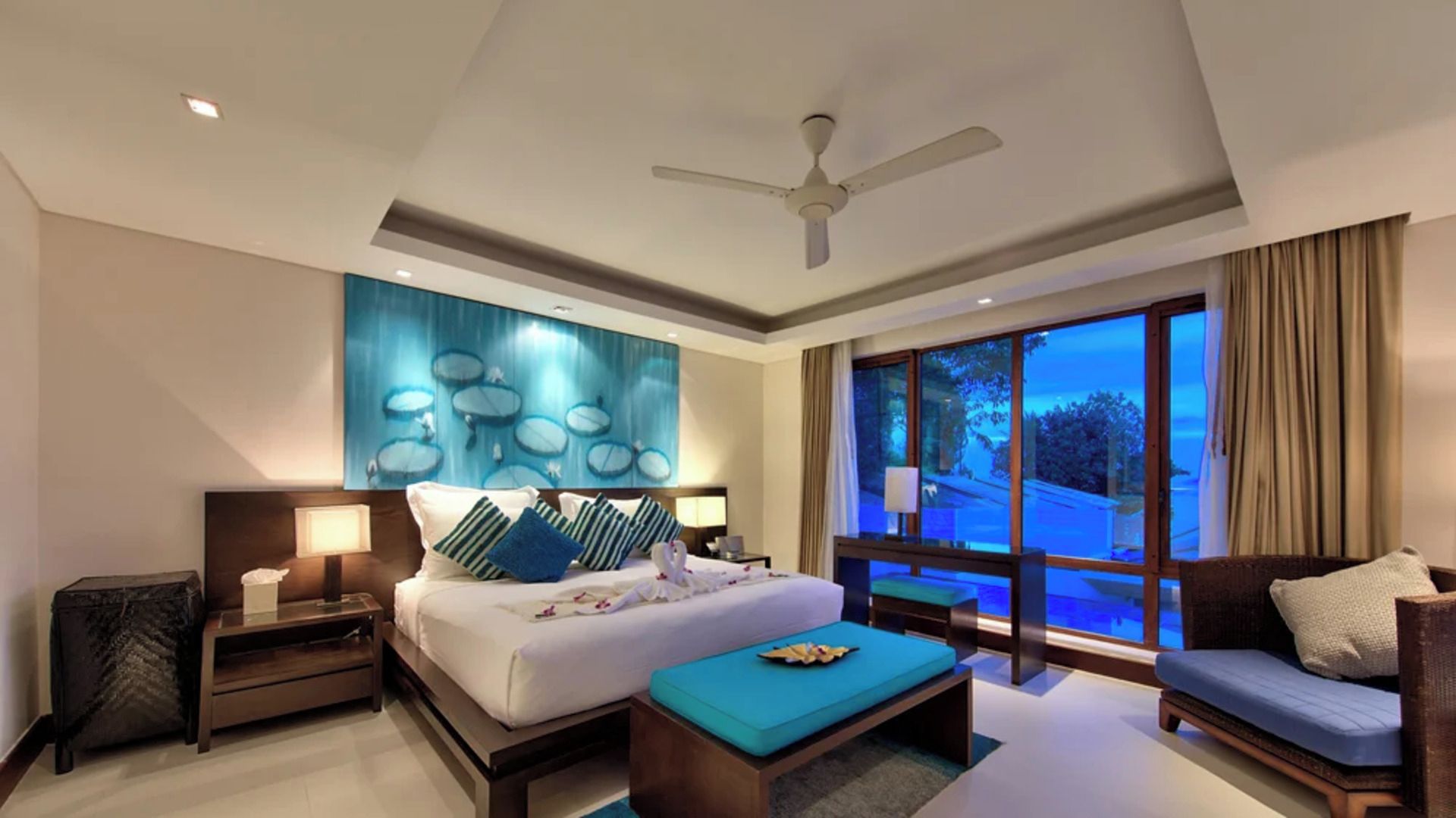 Habitación de hotel con una cama grande, un sofá, una mesa de centro, un ventilador de techo y vistas al exterior.