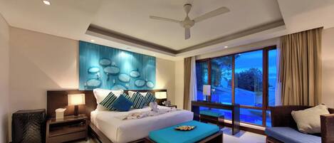 Habitación de hotel con una cama grande, un sofá, una mesa de centro, un ventilador de techo y vistas al exterior.