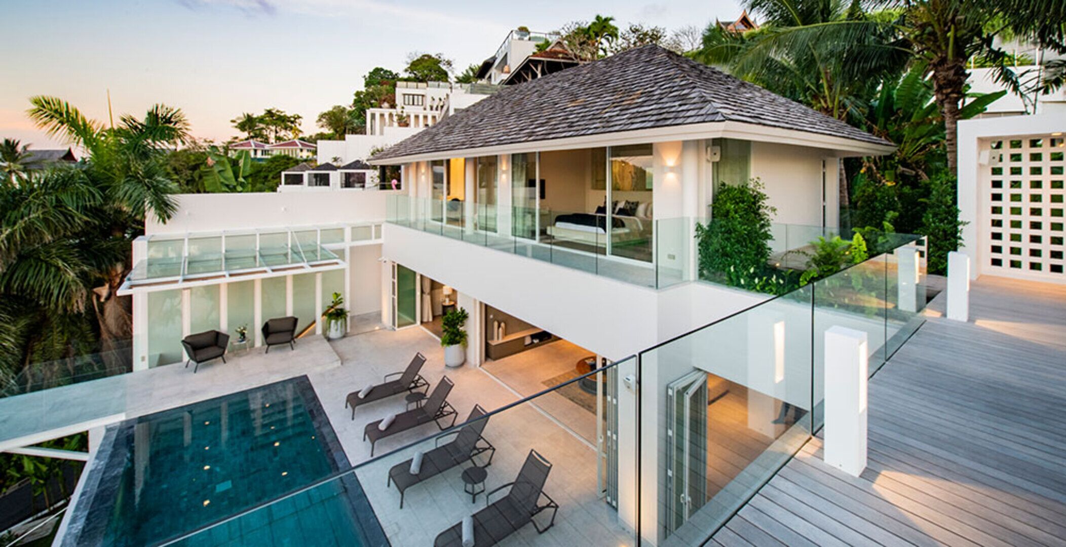 A modern two-story house with a glass balcony, a swimming pool, and outdoor seating.
