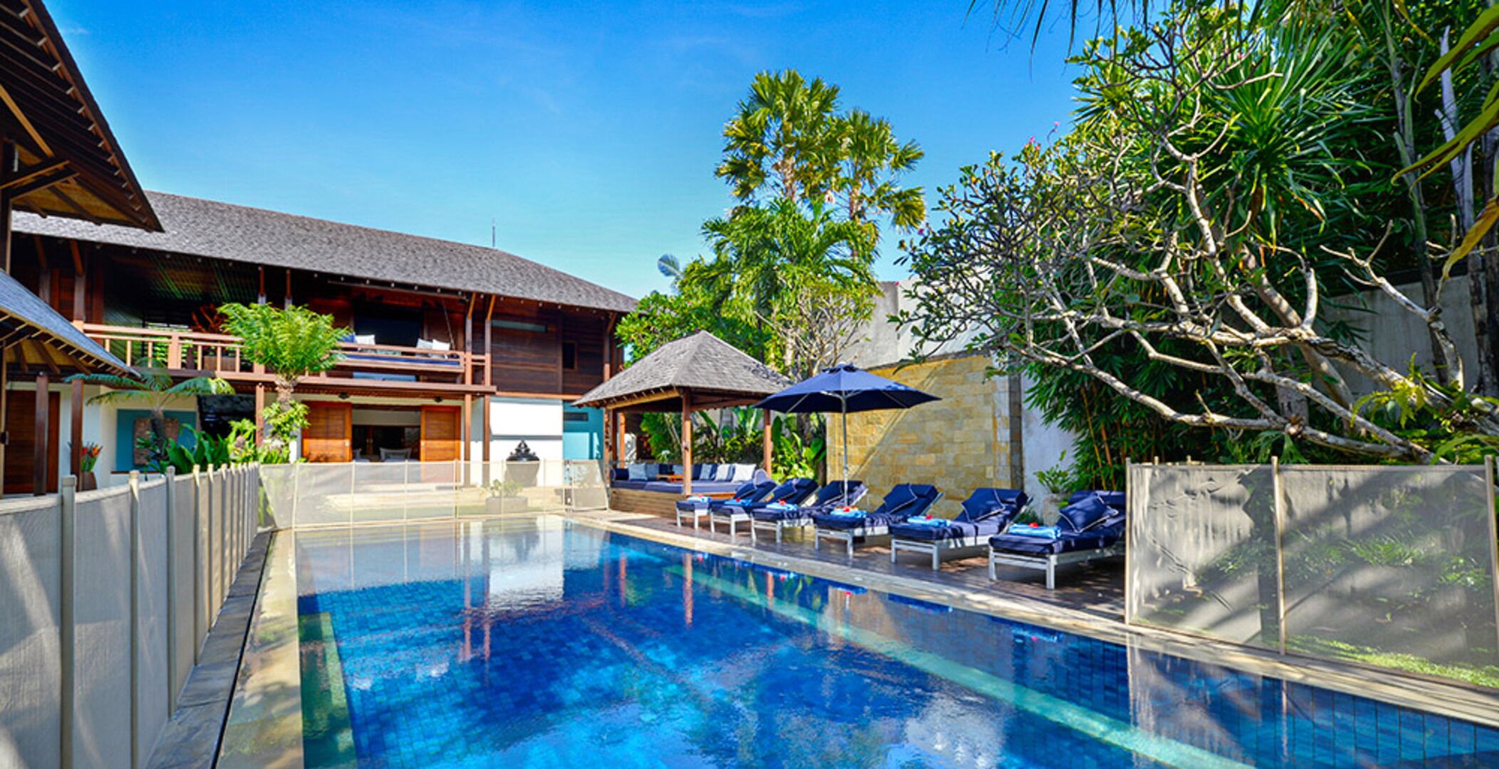 Una piscina con sillones de descanso, un espacio de estar techado y vegetación tropical.
