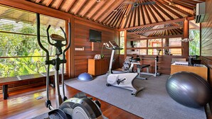 A gym with exercise equipment, a TV, and a view of greenery through large windows. - Beautiful 5 Star Villa in a Prime Location in Seminyak, Bali Villa 2129 (Bali)