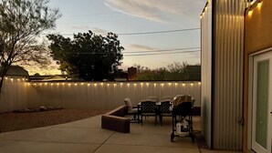 An outdoor patio with a grill, chairs, and a white fence with string lights. - Charming 3-bedroom house in Central location / UofA bike path on Mountain (Tucson)