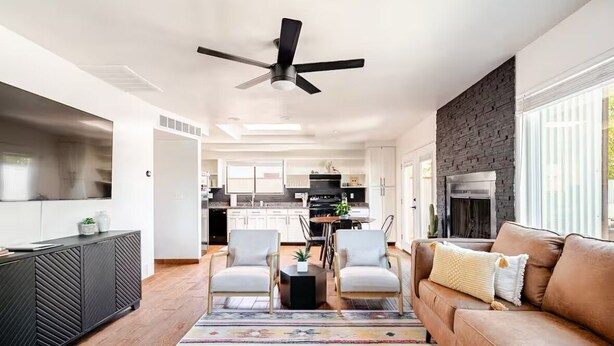 A modern kitchen with white cabinets, a black countertop, and a built-in stove. There is a dining area with a table and chairs, and a living room with a brown sofa and a ceiling fan. - Charming 3-bedroom house in Central location / UofA bike path on Mountain (Tucson)