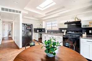 Una cucina moderna con mobili bianchi, piano cottura nero e un lucernario.