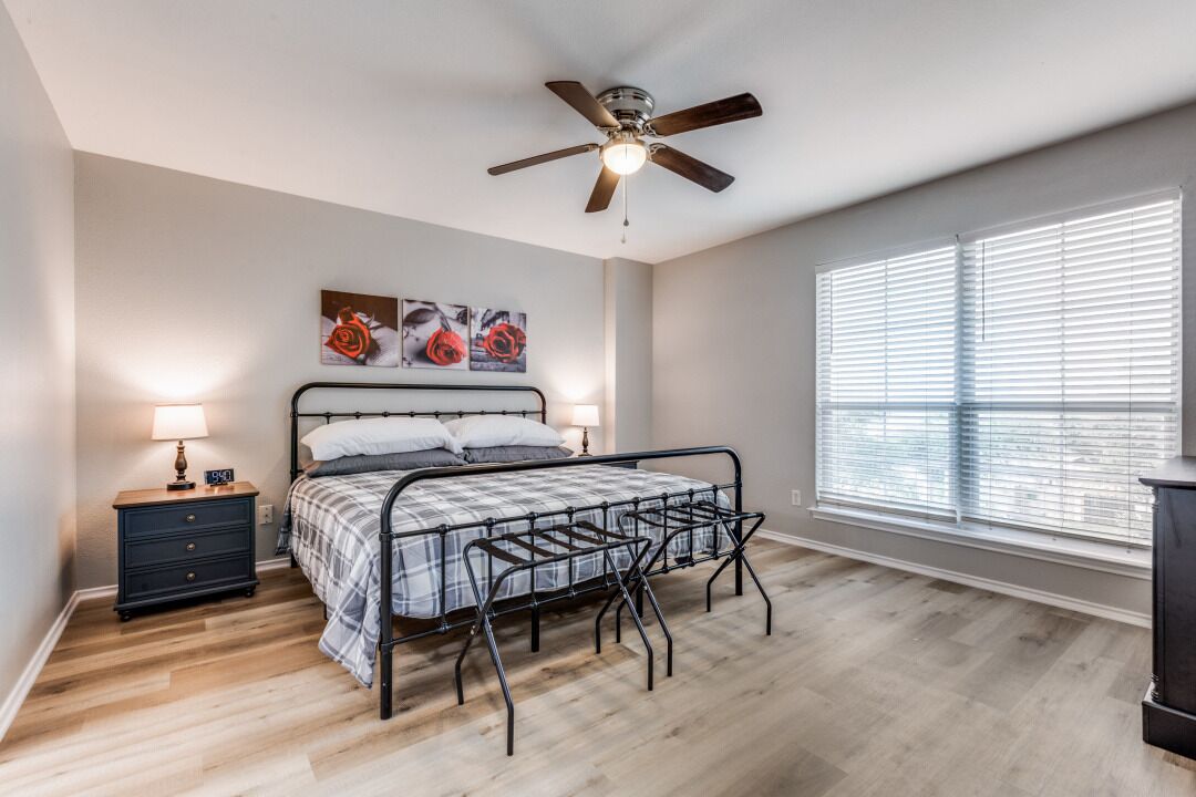 A bedroom with a bed, a nightstand, a ceiling fan, and a window with blinds.