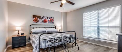 A bedroom with a bed, a nightstand, a ceiling fan, and a window with blinds.