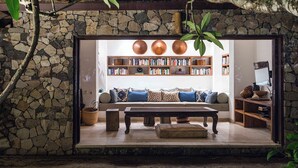 A cozy living room with a stone wall, a sofa, a coffee table, and a bookshelf filled with books.