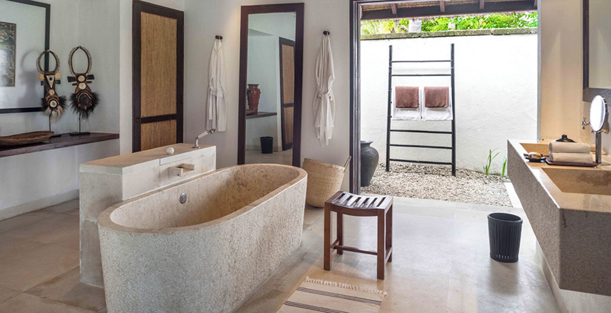 A modern bathroom with a freestanding bathtub, a wooden stool, and a large mirror.