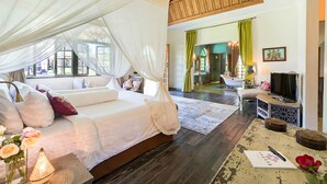 Une chambre à coucher avec un lit à baldaquin, un coin salon avec un téléviseur, et une vue sur une salle de bain et un coin repas.