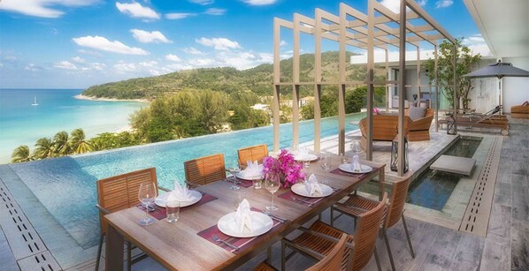 A dining area with a view of a pool and ocean, wooden furniture, and a pergola structure.