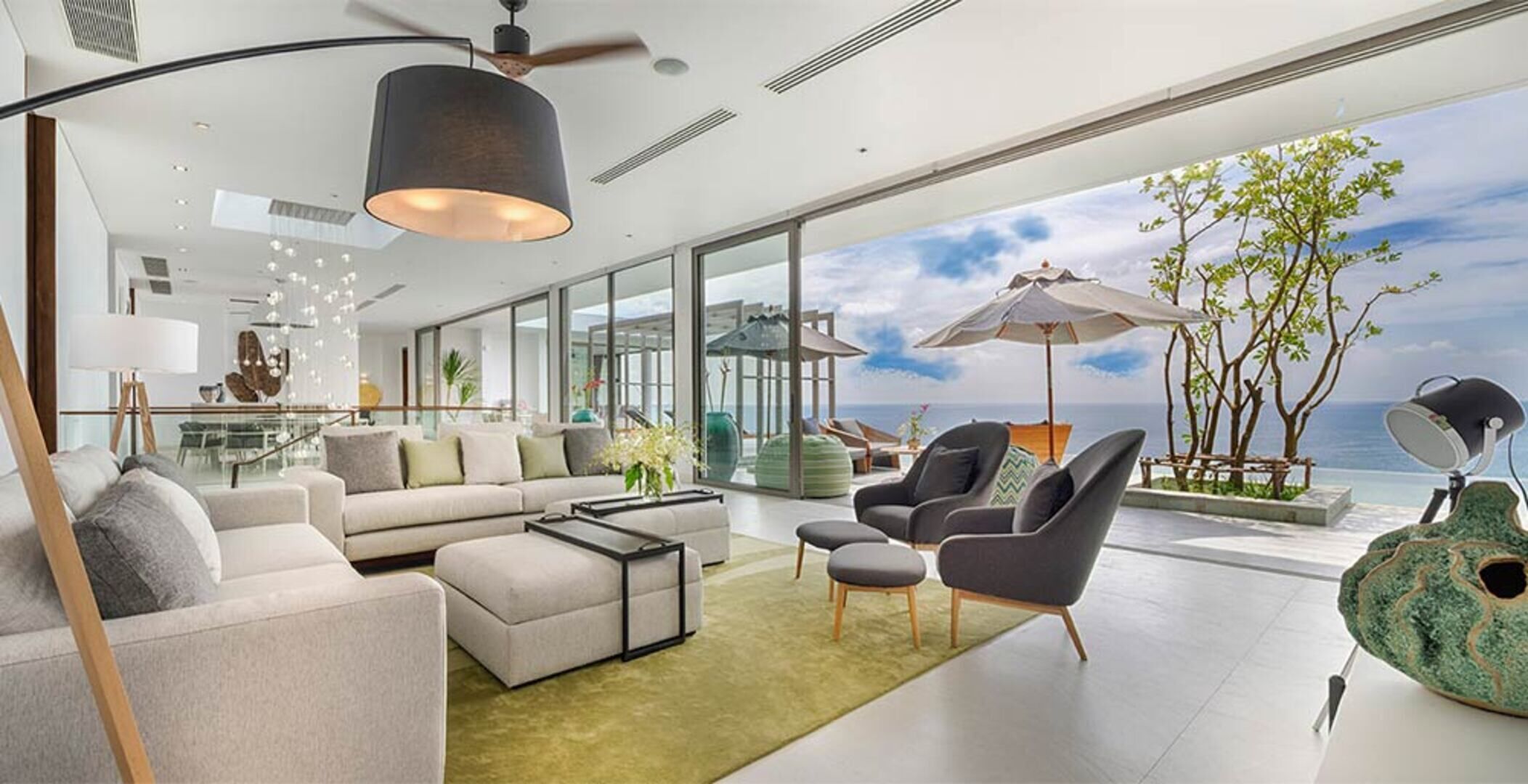 Sala de estar moderna com uma grande janela, ventilador de teto e vista para o mar.